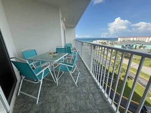 A balcony with a table and chairs, a view of the street, and a building in the background. - 2/2 Ocean front/view, heated pool, snowbird ready (Fort Walton Beach)