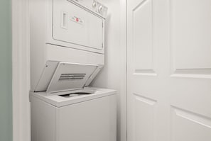 Un appareil compact, blanc, comprenant une laveuse et une sécheuse, fixé au mur dans une petite buanderie dotée d’une porte fermée.