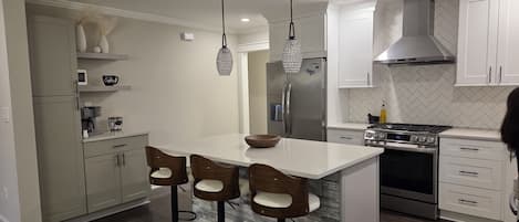 A modern kitchen with a central island, bar stools, stainless steel appliances, and pendant lighting.