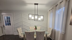 Ein Essbereich mit einem Glastisch, vier gepolsterten Stühlen, einer Chandelierleuchtre und einer Tür mit Fenster.