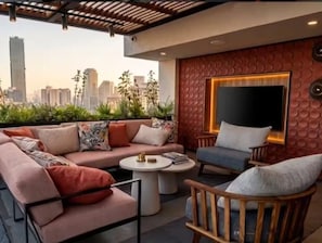 Ein moderner Außenbereich zum Sitzen mit einer Couch und Sesseln, einem runden Tisch und Blick auf die Stadtlandschaft.