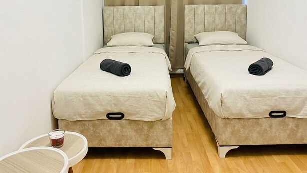 Une petite chambre d’hôtel avec deux lits, une petite table et une fenêtre avec des rideaux.