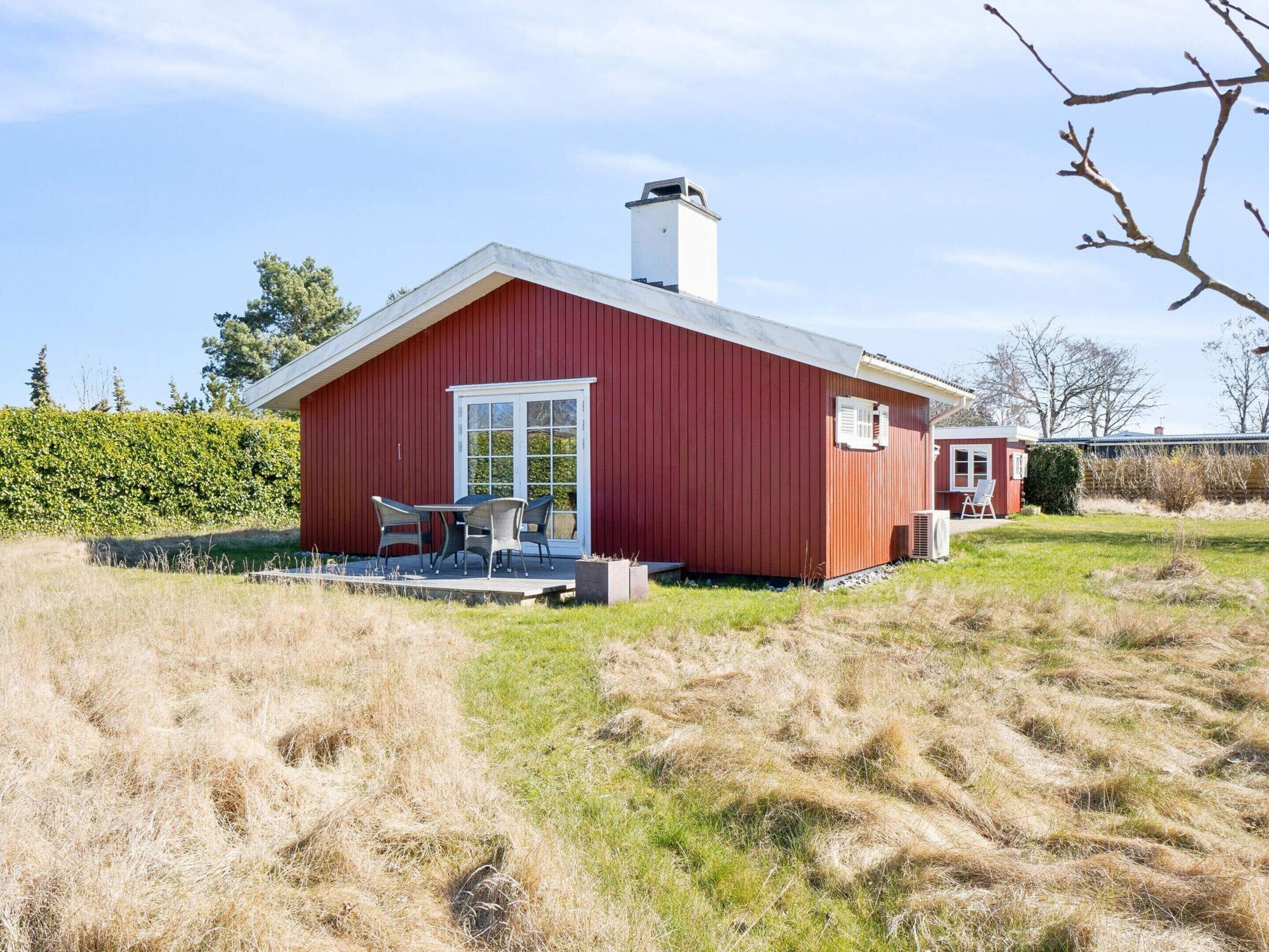 En rød bygning med hvide døre og vinduer, en overdækket terrasse med stole og en græsplæne.