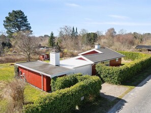 Punavalkoinen rakennus, jossa on kalteva katto, ja sen ympärillä on vehreää kasvillisuutta ja puita.