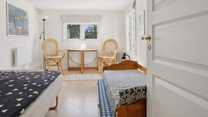 Ein Zimmer mit zwei Betten, einem kleinen Tisch, zwei Korbstühlen und einem Fenster sowie einer Tür.