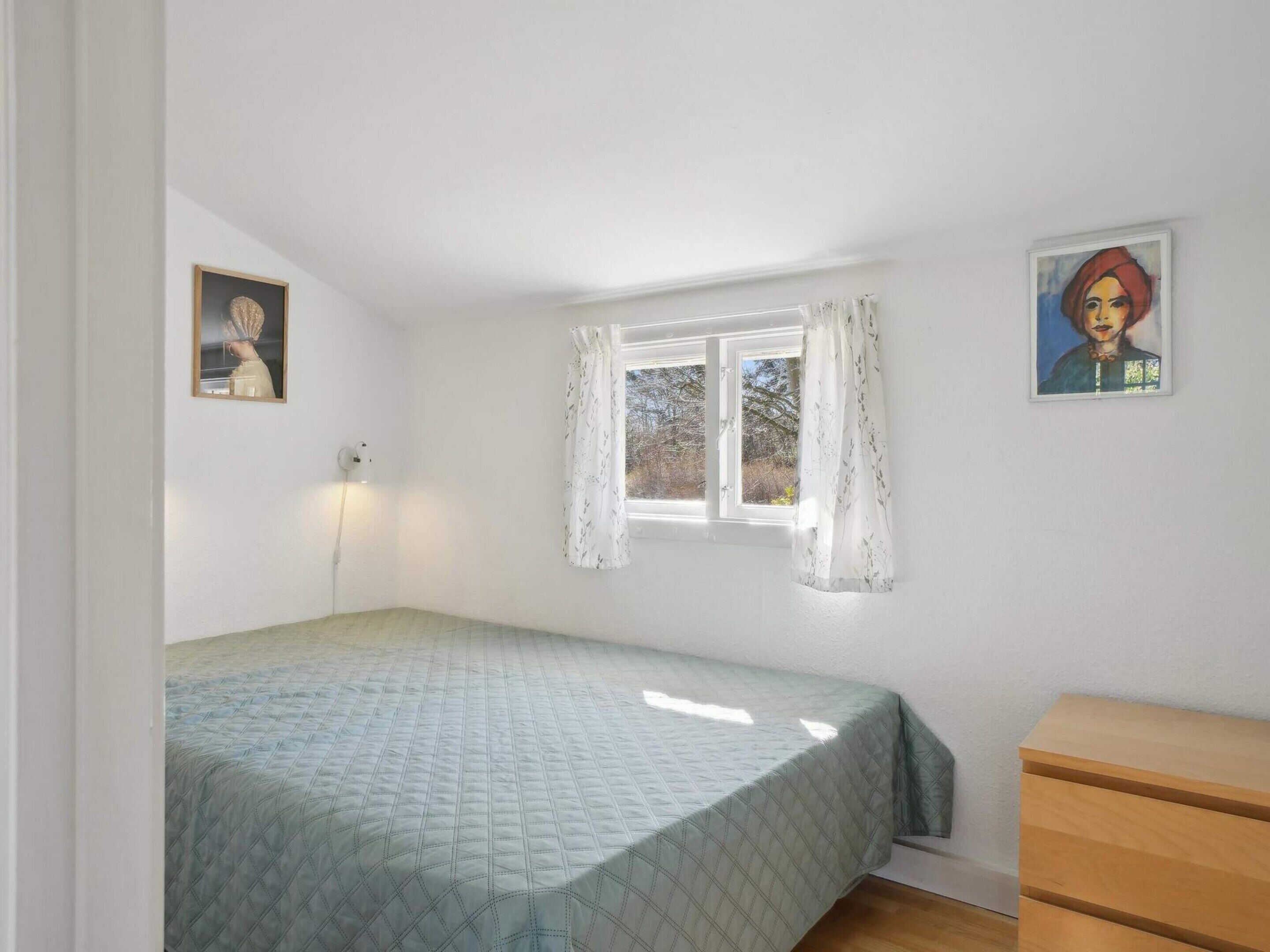 A bedroom with a bed, a window with curtains, a dresser, and two wall-mounted pictures.