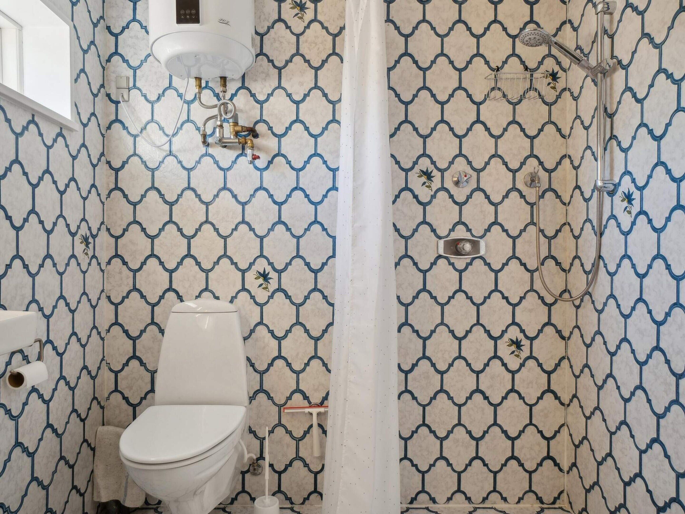 Een badkamer met toilet, douche en een behang met patroon.