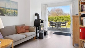Ein Wohnzimmer mit einer Couch, einem Tisch, einem Bücherregal, einem Kamin und einer Terrasse im Freien mit Stühlen und einem Tisch.