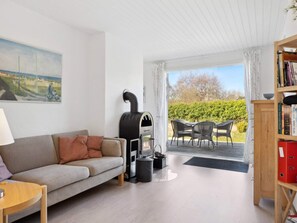 A living room with a sofa, a table, a bookshelf, a fireplace, and an outdoor patio with chairs and a table. - 5 Star Holiday Home in Vejby (Vejby)