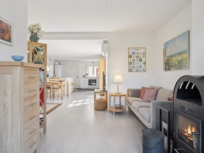 A modern living room with a fireplace, a dining area, and a kitchen in the background. - 5 Star Holiday Home in Vejby (Vejby)