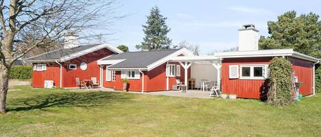 A red building with a covered patio area, a chimney, and a lawn.