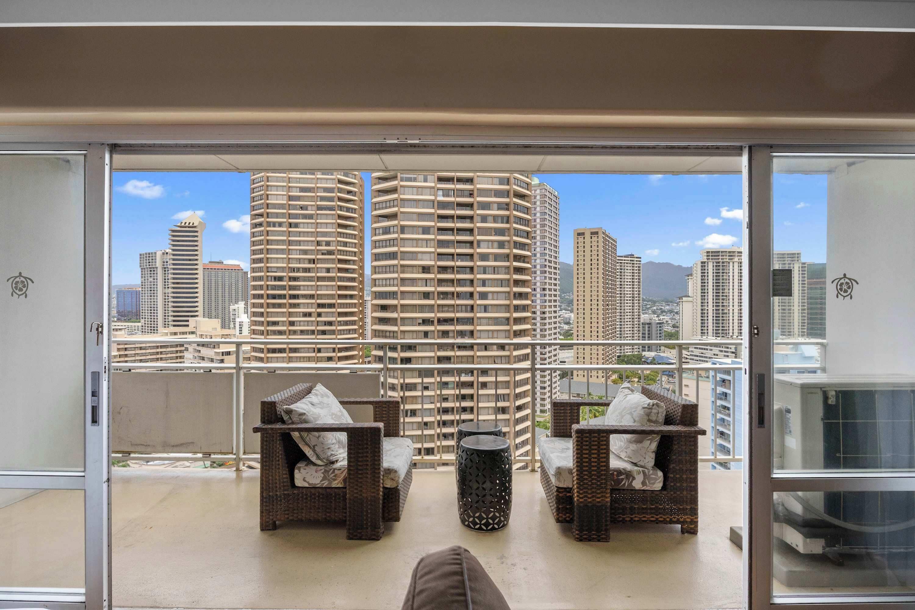 A balcony with wicker furniture, a round table, and a cityscape view.
