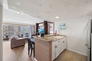 A modern kitchen with a central island, a dining area with a sofa and chairs, and a view of high-rise buildings. - @ Marbella Lane - Iconic Waikiki City View Getaway (Honolulu)