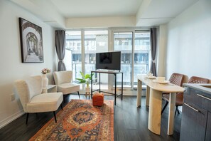 Ett modernt vardagsrum med en soffa, ett soffbord, en TV på ett TV-bord och en matplats med ett bord och stolar.