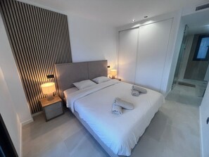 Een moderne slaapkamer met een groot bed, nachtkastjes, een radiator aan de muur en een deur naar een badkamer.