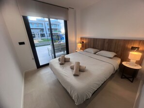 Ein modernes Hotelzimmer mit einem großen Bett, zwei Nachttischen mit Lampen, einem Holz-Kopfteil und einer Schiebeglastür, die auf einen Balkon führt.