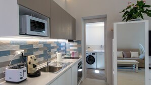 A compact kitchen with a microwave, toaster, sink, and washing machine. - House Salú Suite (Praiano)