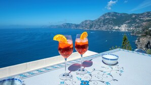 Two glasses of red beverage with orange slices on a table with a decorative border, overlooking a coastal landscape with mountains and the sea. - House Salú Suite (Praiano)