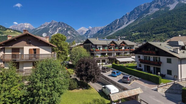 Ein Bergdorf mit traditionellen Häusern, einem Parkplatz und Blick auf die umliegenden Berge.