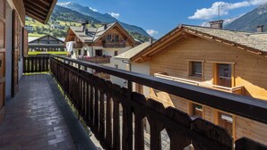 Ein Holzbalkon mit Blick auf ein Bergdorf mit traditionellen Häusern und einem klaren Himmel.