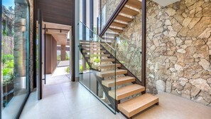 A modern staircase with glass railings and wooden steps, leading to an outdoor area with a stone wall. - Villa The Address by Vacation Marbella (Marbella)