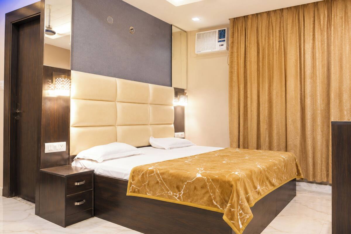 A modern hotel room with a large bed, a dark wooden nightstand, a built-in wardrobe, and a ceiling fan.