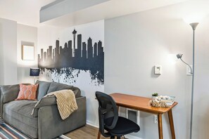 Ein modernes Wohnzimmer mit grauem Sofa, einem Holztisch, einem schwarzen Bürostuhl, einer Stadtblick-Wandmalerei und einer Stehlampe.