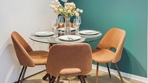 Un comedor moderno con una mesa redonda de vidrio, sillas anaranjadas y una pared de acento color aguamarina.