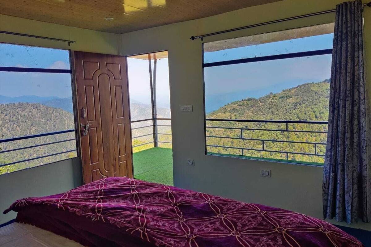 Un dormitorio con cama, puerta de madera y amplios ventanales con vistas a un paisaje montañoso.