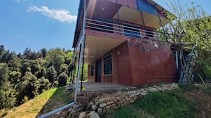 A two-story building with a balcony, surrounded by trees and a stone wall. - Kanatal Greenhood Resort (Kanatal)