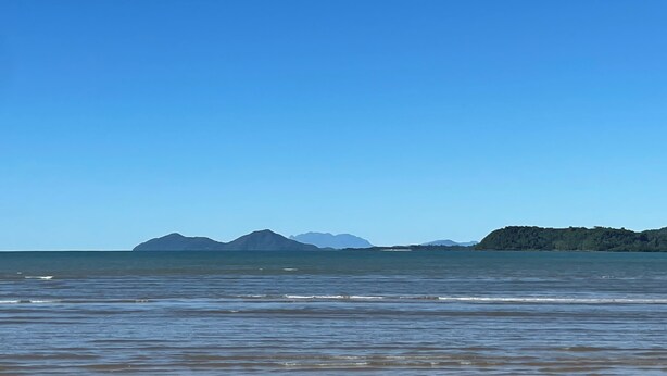 Ein Strand mit ruhigem Wasser und Bergen in der Ferne.