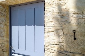 Una puerta con paneles verticales, un ojo de cerradura y una pared de piedra texturizada.