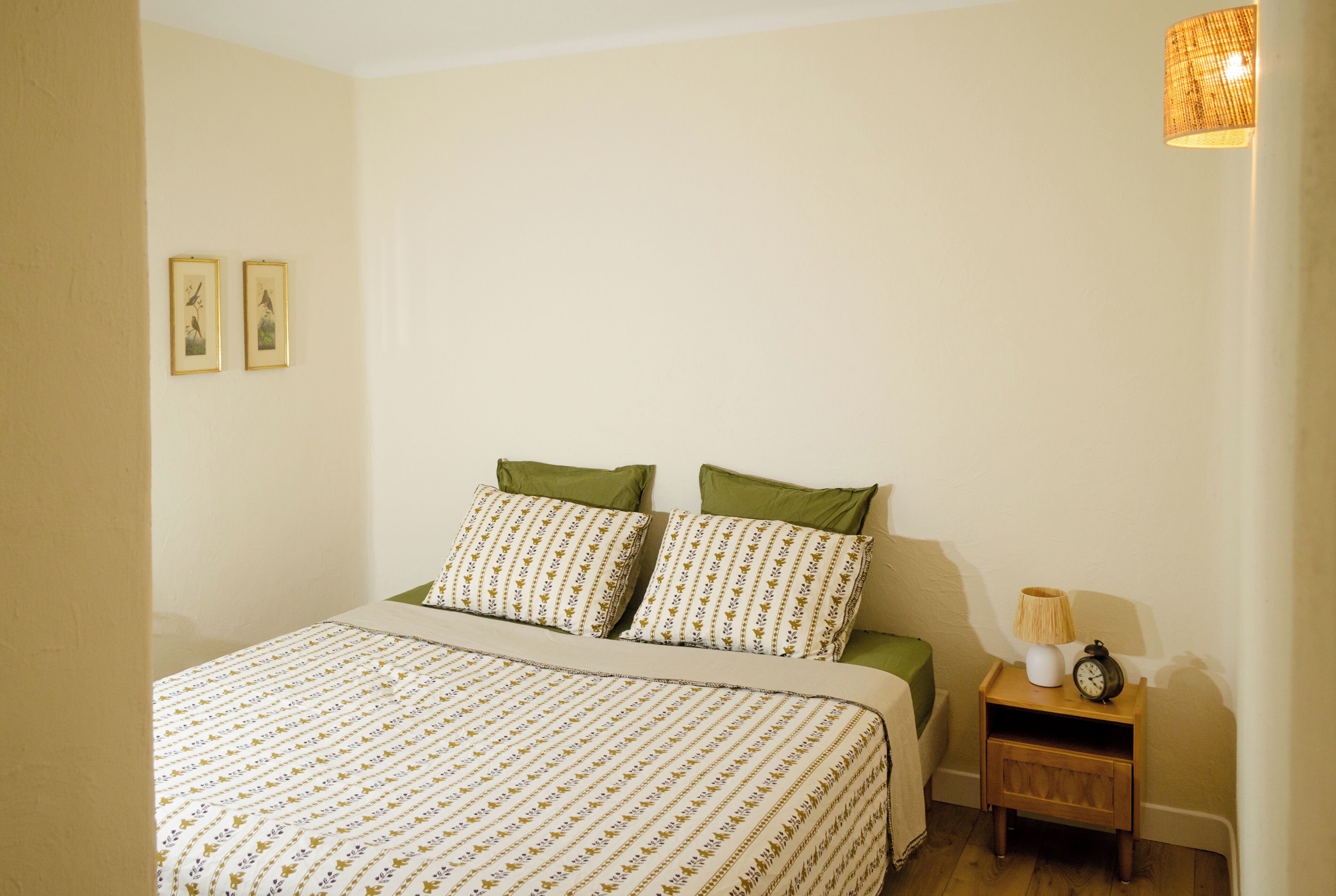 A bedroom with a bed, pillows, a nightstand, a lamp, and two framed pictures on the wall.