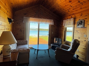 A cozy cabin interior with a wooden ceiling, a sofa, a chair, a table, and a TV. - Drummond Island Hotel & Vacation Homes - Kaye's Little Cabin (Drummond)