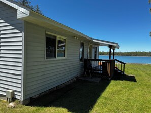 A single-story house with a covered porch, a small deck, and a view of a lake.