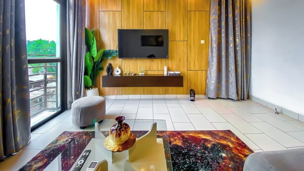 Ett modernt vardagsrum med en stor TV, väggar beklädda med träpaneler, ett soffbord i glas och en utsikt genom ett stort fönster.