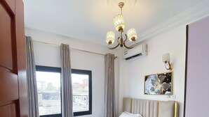 Ett hotellrum med en säng, gardiner, en kristallkrona, en luftkonditioneringsanläggning och ett fönster med utsikt.