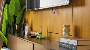 Ett modernt vardagsrum med en tv som är monterad på en vägg av trä, en stor krukväxt, en vit vas och ett litet bord med en bok som heter ”Dior”.