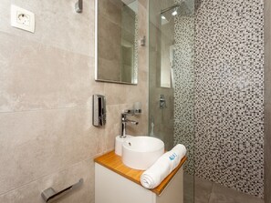 Ein Badezimmer mit Waschbecken, Spiegel, Handtuch und Duschbereich.