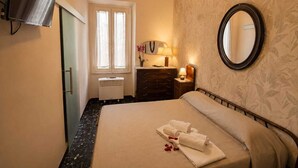 A hotel room with a bed, a dresser, a mirror, a window with curtains, a wall-mounted TV, and a ceiling light. - Boutique Hotel Golfo Azzurro (Capoliveri)