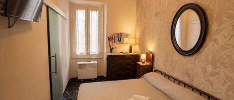 A hotel room with a bed, a dresser, a mirror, a window with curtains, a wall-mounted TV, and a ceiling light.