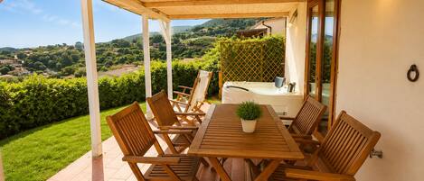 An outdoor patio with a wooden table and chairs, a hot tub, and a view of the countryside.