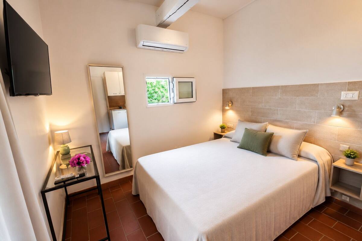 Habitación de hotel con cama, mesitas de noche, televisión, espejo y ventana.