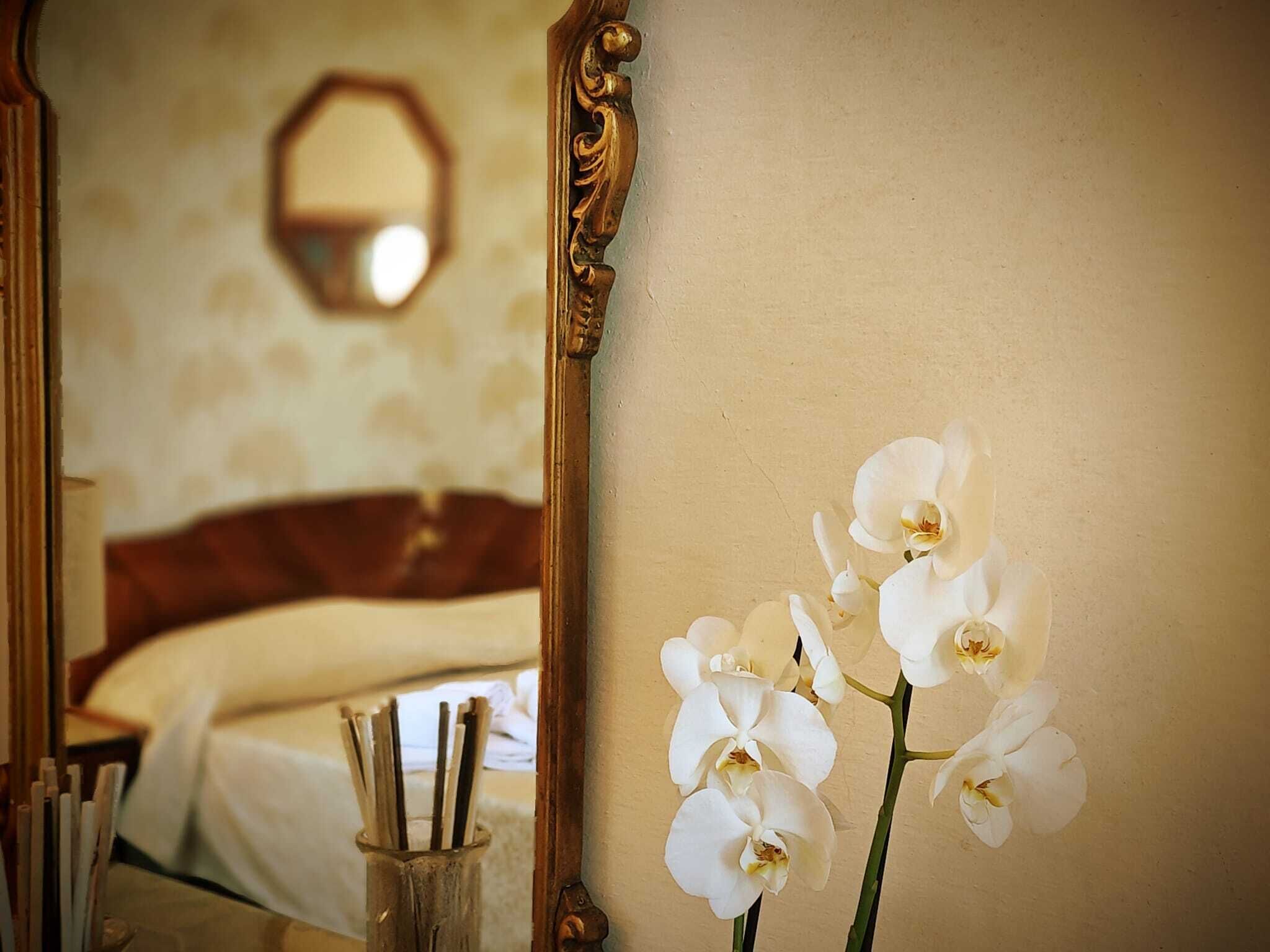 A mirror reflecting a bed and a vase with white flowers.