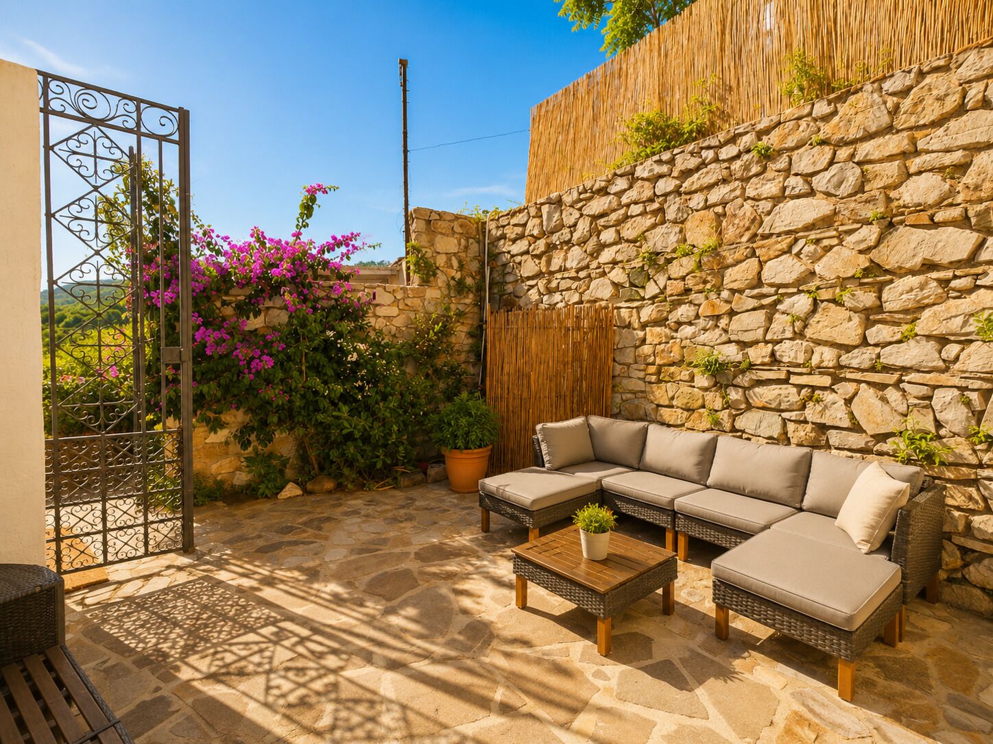 A stone wall, a wrought iron gate, a wicker sofa, and a potted plant.