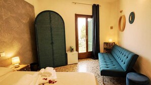 A hotel room with a bed, a blue sofa, a large arched door, a small table with a lamp, and a window with curtains. - Boutique Hotel Golfo Azzurro (Capoliveri)