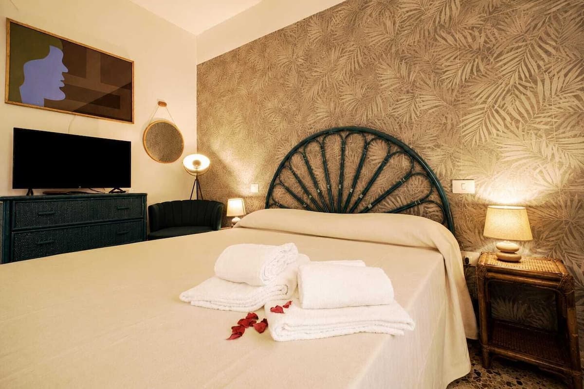 Habitación de hotel con una cama, televisión, espejo y una pared decorada con un diseño de hojas.