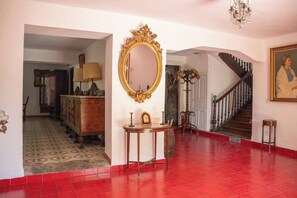 Un passadís espaiós amb sòl de rajola vermella, un gran mirall amb detalls decoratius, una escala i un penjador.