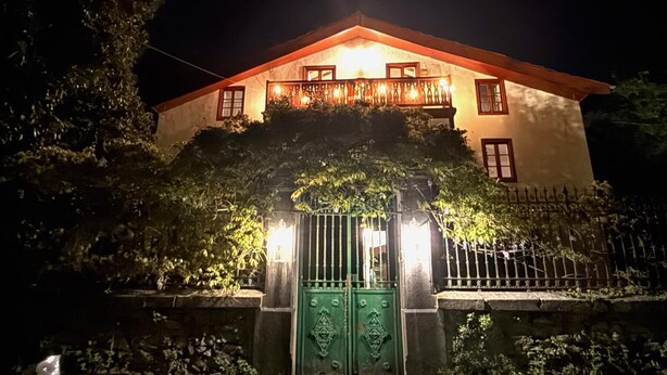 Une maison à deux étages avec un balcon, une entrée fermée par un portail et un mur de pierre à l’avant.