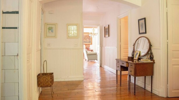Un couloir doté d’un plancher en bois, de murs blancs, d’une commode en bois avec un miroir et de tableaux encadrés.